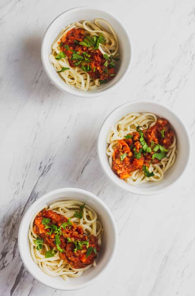 three white bowls of vegan Lentil Bolognese served over pasta and topped with parsley