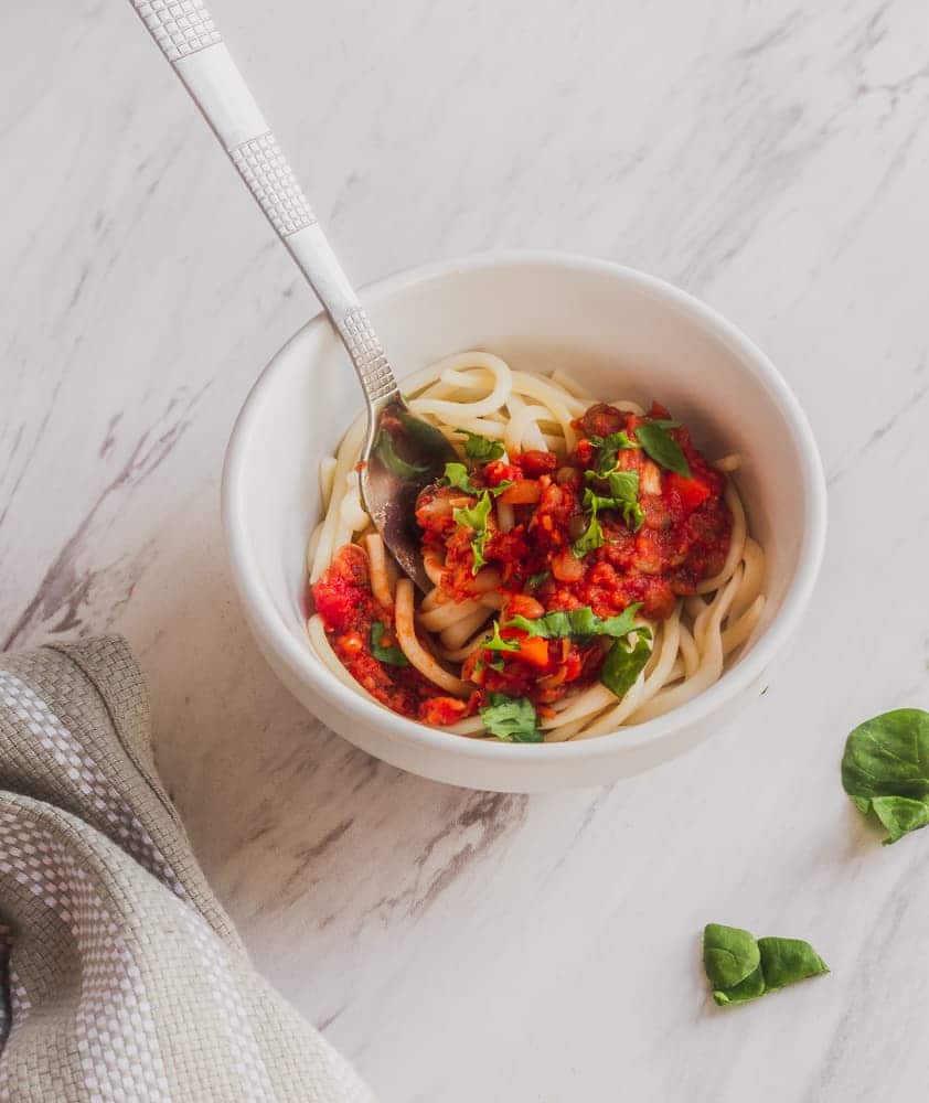 white bowl of lentil bolognese with fork topped with parsley