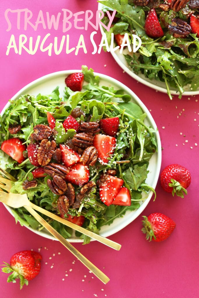 arugula salad with candied pecans, strawberries, hemp seeds on white plate