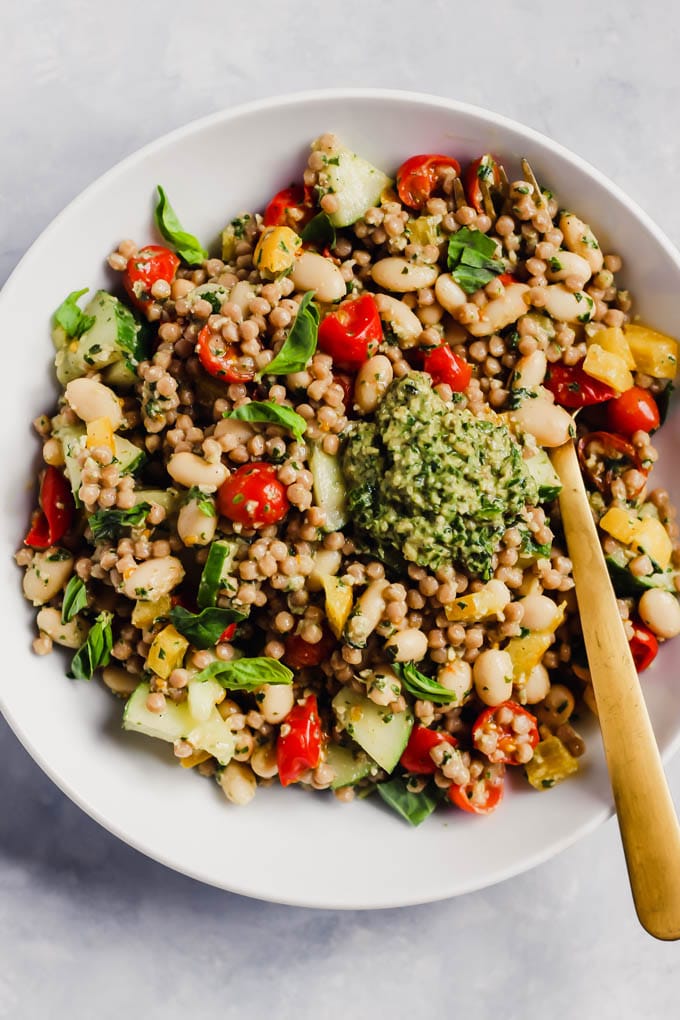 couscous with tomatoes, bell peppers, white beans, and pesto in a white bowl