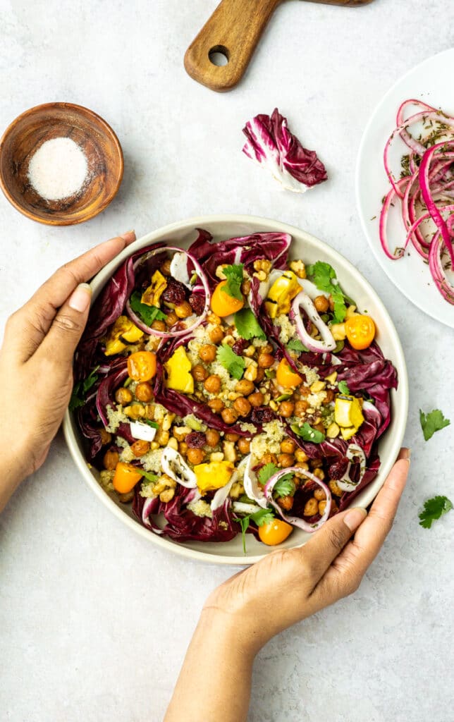 winter salad recipe with radicchio, marinated onions, chickpeas, squash, tomatoes, in tan bowl with wooden cutting board