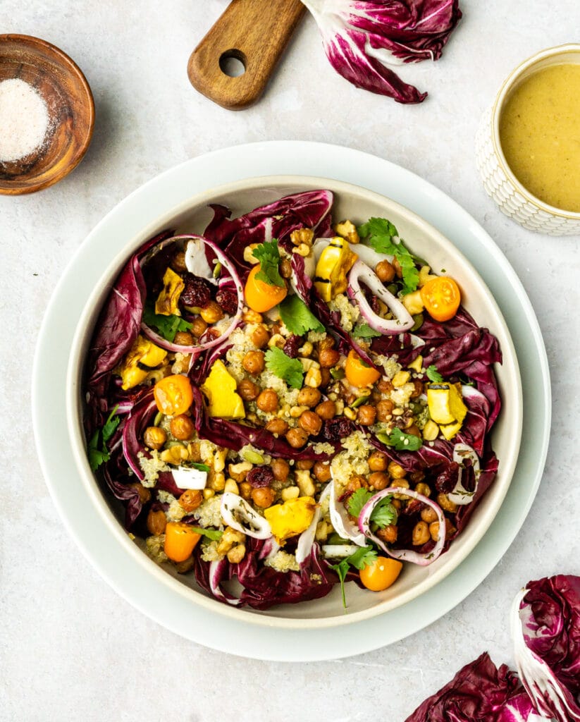 winter salad with radicchio, chickpeas, squash, tomatoes, quinoa, citrus vinaigrette, in tan bowl